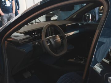 Innenansicht eines Autos von Lancia Nederland mit einem Lenkrad mit digitalem Armaturenbrett und minimalistischen Designelementen.