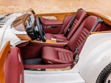 Un elegante interior de coche con asientos de cuero rojo, salpicadero de madera y un moderno volante, que recuerda a una mezcla británico-italiana de elementos de diseño clásicos y contemporáneos.