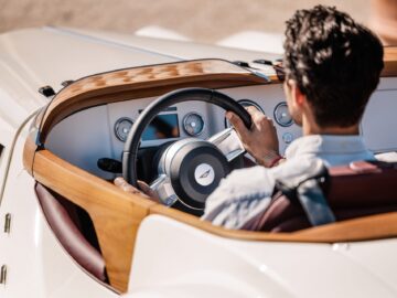 Persoon die een vintage auto bestuurt met een houten dashboard en stuur, van achteren gezien, met klassieke Brits-Italiaanse schoonheid.