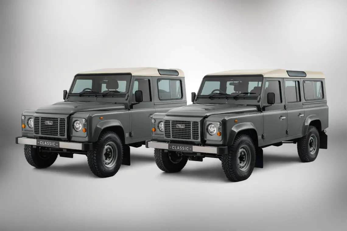 Zwei graue, klassische Geländewagen mit weißen Dächern sind nebeneinander in einer Studioumgebung geparkt, die die Atmosphäre einer aufregenden Safari heraufbeschwört. Man kann sich leicht vorstellen, dass diese Land Rover-Klassiker oder sogar ein neuer Defender unwegsames Gelände mit Leichtigkeit bewältigen könnten.