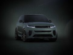 Een donkergekleurde Range Rover SUV is van voren afgebeeld tegen een donkere achtergrond. Het voertuig, één van de nieuwe uitvoeringen, is voorzien van strakke koplampen en een opvallende grille.