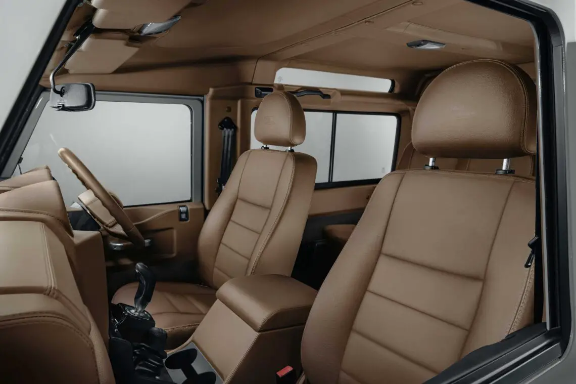 Vue de l'intérieur d'une Land Rover Classic avec des sièges en cuir marron, un volant et un tableau de bord au design minimaliste avec beaucoup d'espace pour les jambes, parfait pour une aventure en safari.