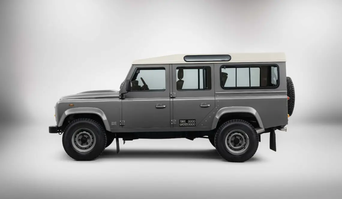 Un Land Rover Defender 110 gris avec un toit blanc est présenté dans un studio. Cette Land Rover Classic est équipée d'une roue de secours à l'arrière, prête pour votre prochaine aventure en safari.