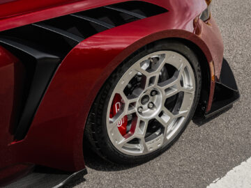 Nahaufnahme des Vorderrads eines roten Ford Mustang GTD mit verschlungenen silbernen Leichtmetallfelgen, schwarzen aerodynamischen Merkmalen und sichtbaren roten Bremssätteln, geparkt auf einer gepflasterten Fläche.