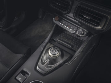 Close-up van de middenconsole van een Ford Mustang GTD met een draaiknop voor de versnellingspook, een reeks knoppen, ventilatieopeningen en gestructureerde oppervlakken. Het interieur heeft een strak, modern design met donkere afwerkingen die passen bij de premium prijzen van de auto.