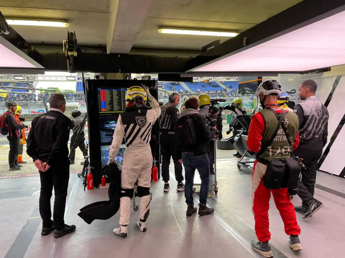 Bemanningsleden in een racegarage houden schermen in de gaten en werken aan apparatuur terwijl ze zich voorbereiden op de komende 24 uur van Le Mans, en leggen de intensiteit van deze één keer in je leven-ervaring vast.