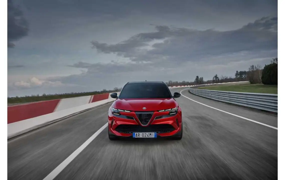 A red Alfa Romeo Junior driving on a race track, with an overcast sky in the background.
