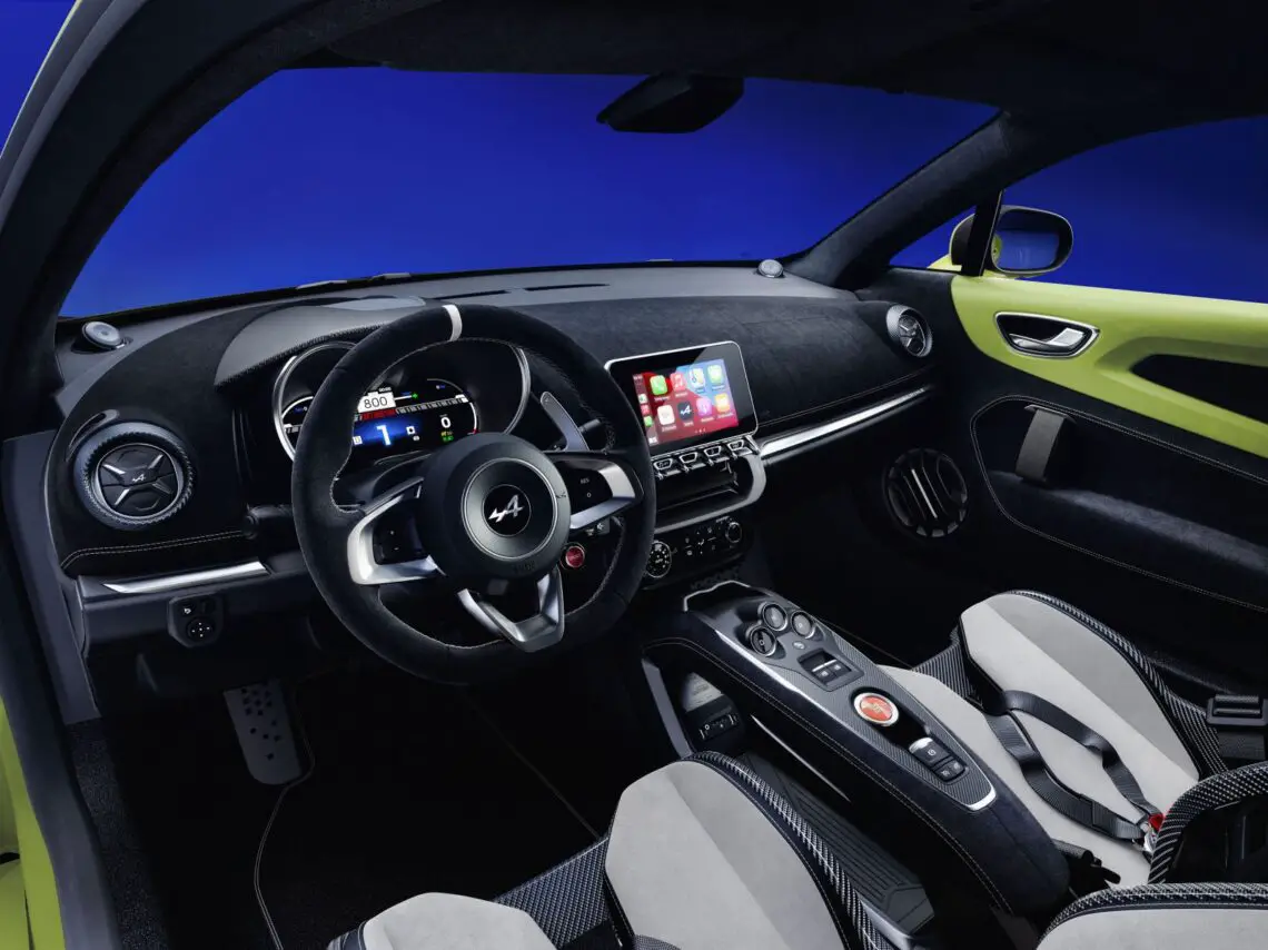 Binnenaanzicht van een moderne Alpine A110 met zwarte en grijze stoelen, een multifunctioneel stuur, een digitaal dashboard en een touchscreendisplay op de middenconsole. De auto is voorzien van het exclusieve personalisatieprogramma tegen een blauwe achtergrond.