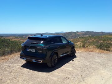 Een zwarte Nissan Qashqai staat geparkeerd op een onverharde weg met uitzicht op een uitgestrekt landschap van heuvels en helderblauwe luchten.