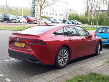 A red Toyota Mirai is spotted on the side of a street with other vehicles nearby.