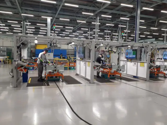 Werknemers assembleren machines op een productielijn in een helder verlichte fabriek in Sunderland, met verschillende gereedschappen, schermen en uitrustingsstations. De vereiste precisie weerspiegelt de toewijding die te zien is bij de productie van de Nissan Qashqai.