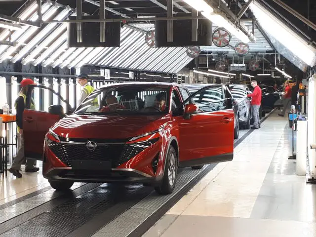 Un Nissan Qashqai rouge est assemblé sur une ligne de production à l'usine de Sunderland. Des ouvriers sont visibles à l'arrière-plan, s'occupant de différentes parties du véhicule.