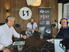 Drie mannen zitten rond een tafel voorzien van microfoons en koptelefoons en nemen een aflevering op van de AutoRAI Podcast. Achter hen staat een bord met de tekst 