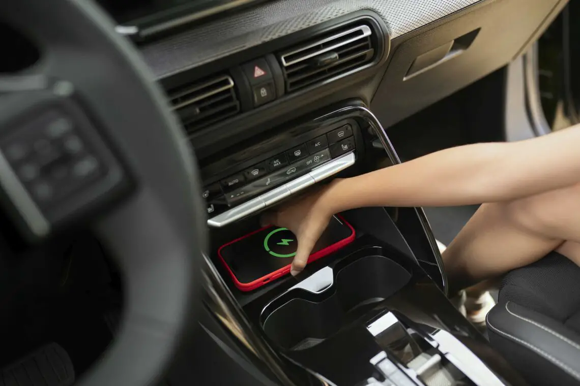 Persoon die een smartphone op een draadloos oplaadstation in de middenconsole van de Citroën (ë)-C3 Aircross plaatst. De telefoon geeft een oplaadsymbool weer.