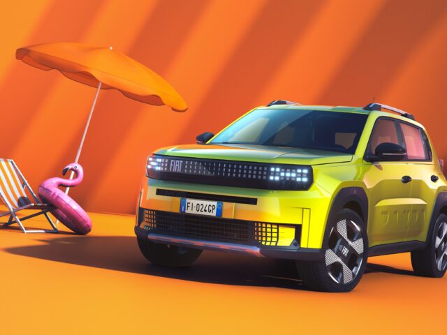 Een felgele Fiat Grande Panda SUV staat geparkeerd naast een oranje parasol, een strandstoel en een roze opblaasbare flamingo, allemaal tegen een oranje achtergrond.