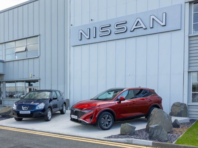 Twee auto's, een zwarte SUV en een rode Nissan Qashqai, staan geparkeerd buiten een gebouw met een groot bord 'Nissan'. Deze voertuigen zijn onlosmakelijk verbonden met het trotse automobielerfgoed van Sunderland.