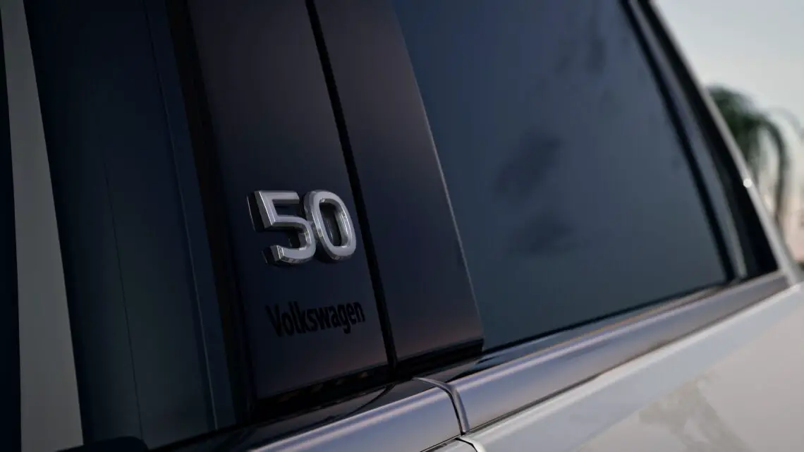 Close-up van de zuil van een Volkswagen Golf met een chroom '50'-embleem en 'Volkswagen'-tekst eronder, wat de verfijnde details benadrukt die dit EV-model onderscheiden.