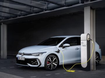Een witte Volkswagen Golf EV wordt aangesloten op een laadstation onder een overdekte ruimte, waardoor het rijbereik wordt geoptimaliseerd.