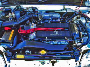 Un moteur de Honda CR-X avec des fils d'allumage rouges dans un capot ouvert, révélant divers composants tels que la batterie, l'admission d'air et le radiateur.