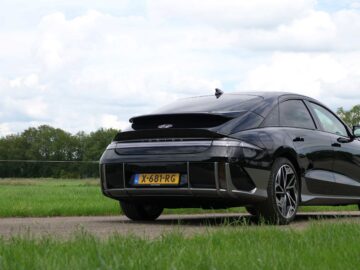 Op een verharde weg naast een grasveld onder een halfbewolkte hemel staat een strakke zwarte Hyundai IONIQ 6 sedan met geel kenteken geparkeerd, klaar om te pronken met zijn indrukwekkende actieradius van 600 kilometer en snelladende capaciteiten.