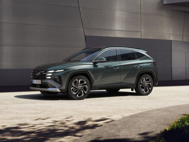 Een donkergroene Tucson SUV geparkeerd op een lichtgekleurd oppervlak voor een modern gebouw met metaalgrijze buitenmuren.