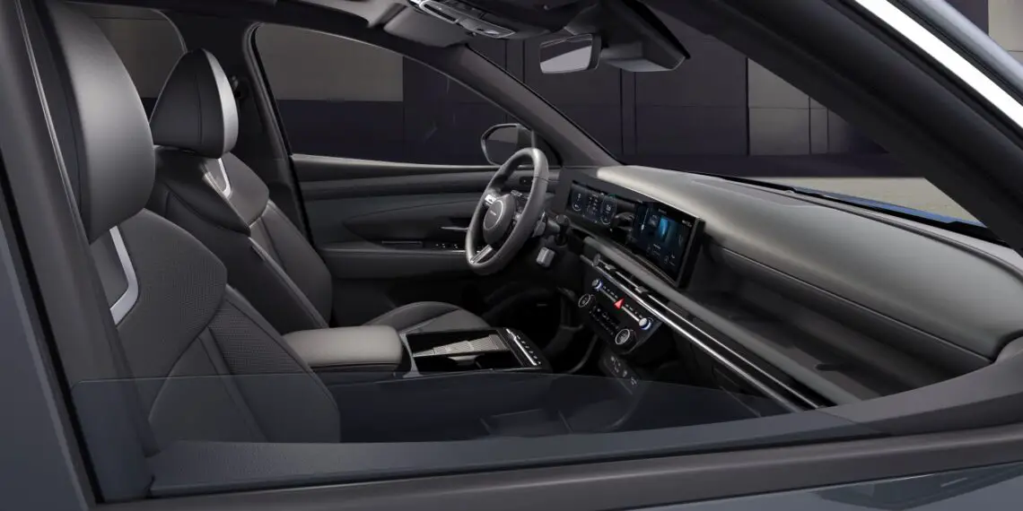 Interieur van een moderne Hyundai Tucson met de voorstoelen, het stuur, het bedieningspaneel met schermen en de middenconsole met versnellingspook. Het ontwerp is strak en eigentijds en weerspiegelt de laatste facelift voor een frisse, nieuwe look.