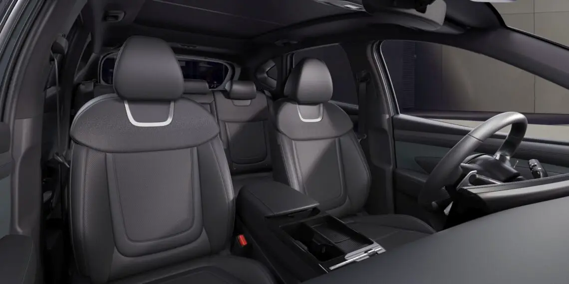 Een modern auto-interieur met twee grijze stoelen vooraan, een middenarmsteun en een dashboard met stuur. De deurpanelen en achterbank van de gefacelifte Hyundai Tucson zijn ook zichtbaar, wat het nieuwe ontwerp laat zien.