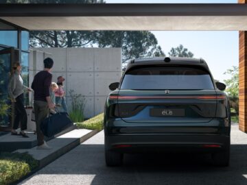 A family prepares to load luggage into a black SUV parked in the driveway of a modern home.