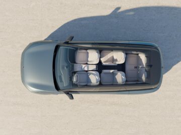 Vue de dessus d'un véhicule à toit transparent, avec trois rangées de sièges et un aménagement intérieur spacieux. L'extérieur de la voiture est gris.