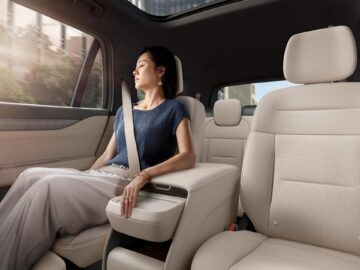 Une femme portant une ceinture de sécurité dort sur le siège arrière d'une voiture dotée d'un grand toit ouvrant par une journée ensoleillée.