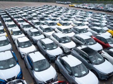 Een grote parkeerplaats in Sunderland staat vol met rijen nieuwe auto's, waaronder witte, zilveren en een paar blauwe en gele voertuigen. Onder hen valt de Nissan Qashqai op, die onlosmakelijk verbonden is met de auto-erfenis van de stad.