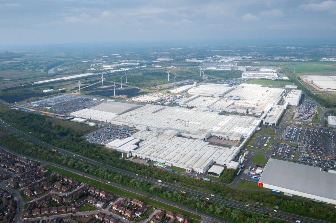 Luchtfoto van het grote industriële complex van Sunderland, met talloze gebouwen met witte daken en groene velden bezaaid met windturbines. Nabijgelegen woonwijken en de productielocatie voor de Nissan Qashqai completeren dit dynamische landschap.