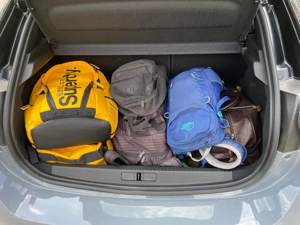 A trunk containing a yellow duffel bag, a gray backpack, a black backpack, a blue backpack and a brown leather bag: perfectly packed for your long road trip in the compact and efficient Opel Corsa Electric.