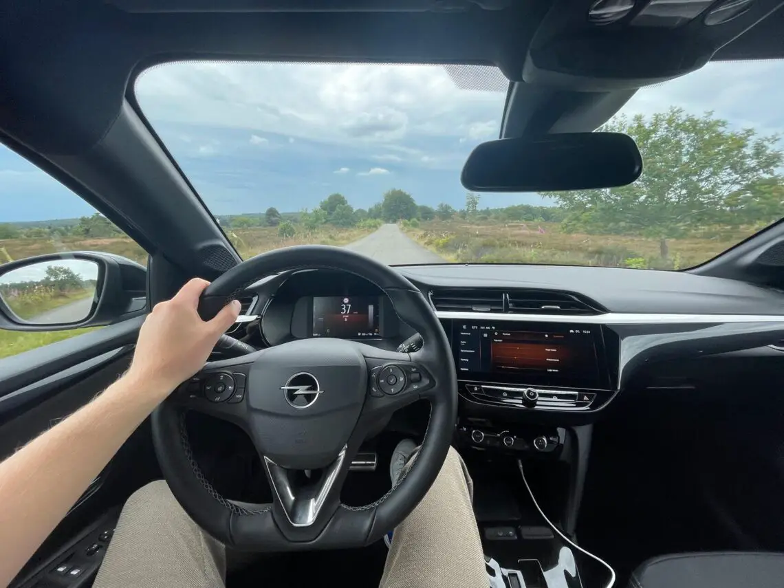 Blick aus der Fahrerperspektive in einem Opel Corsa Electric, der an einem bedeckten Tag das Lenkrad, das Armaturenbrett und einen weiten Blick durch die Windschutzscheibe zeigt.