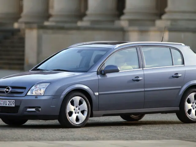 A silver Opel Signum station wagon is parked in a paved lot in front of a historic building with columns, clearly spotted for its elegance and classic charm.