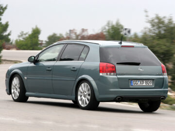 A gray Opel Vectra Stationwagon, almost mistaken for an Opel Signum, was seen driving on a road, seen from behind with trees and bushes in the background.