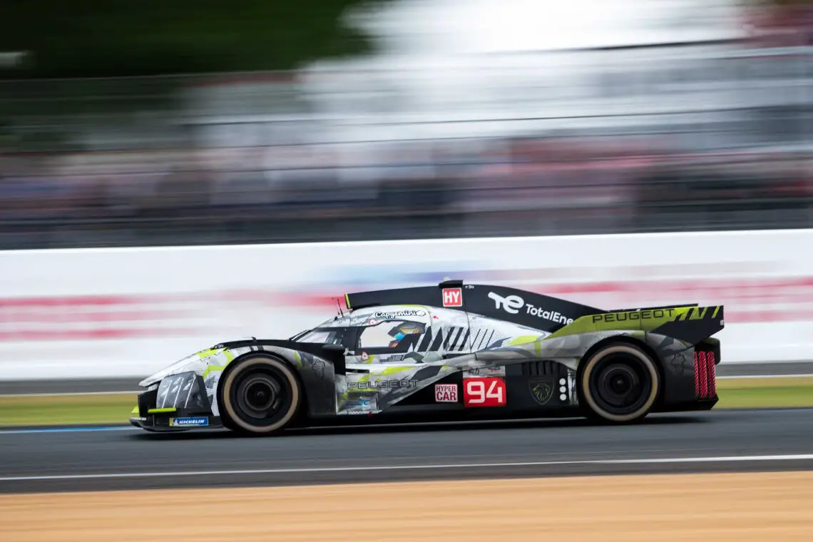 Een Peugeot 9X8-raceauto met het nummer 94 snelt tijdens een race over een circuit, waarbij bewegingsonscherpte een hoge snelheid aangeeft. De auto is voorzien van logo's en branding van sponsors.