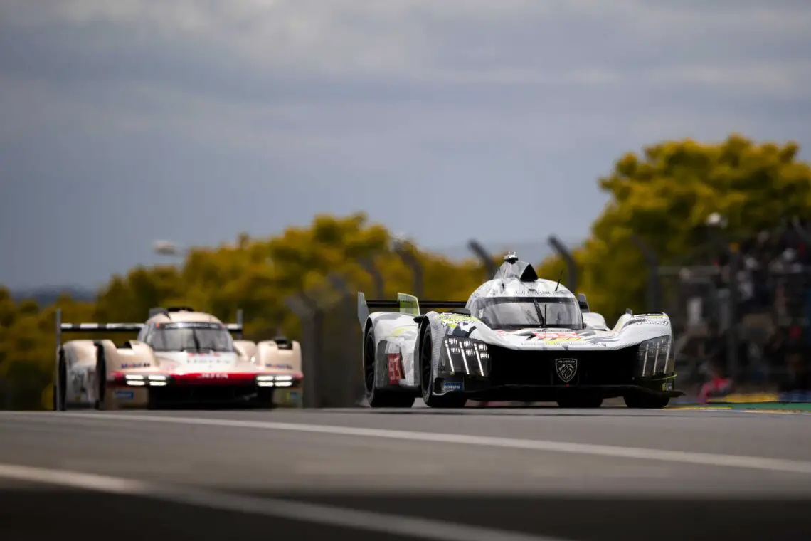 Twee raceauto's strijden op een circuit, één op de voorgrond en de andere erachter – een slanke Peugeot 9X8 – te midden van bomen en toeschouwers onder een bewolkte hemel.