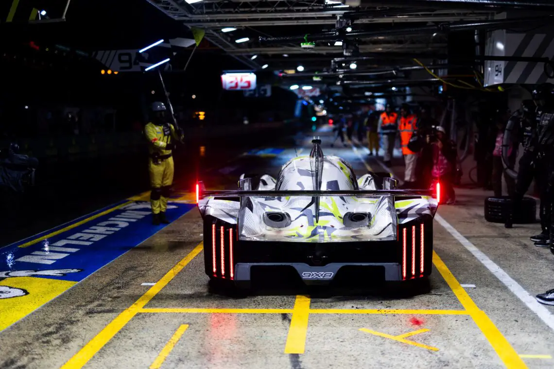 Een Peugeot 9X8-raceauto krijgt 's nachts onderhoud in een goed verlichte pitstop, terwijl bemanningsleden eromheen werken en de achterlichten branden.