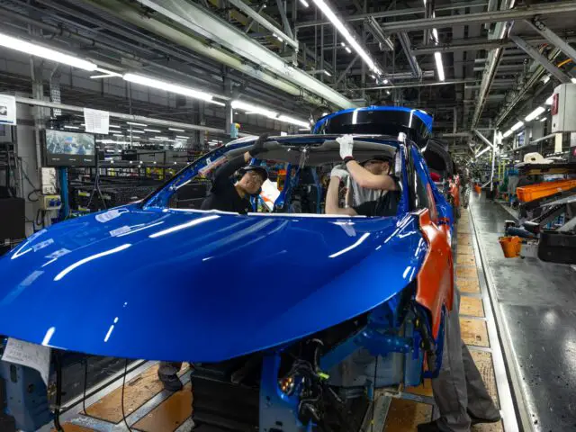 Twee arbeiders monteren nauwgezet een blauwe Nissan Qashqai op een autoproductielijn in Sunderland, omringd door machines en gereedschappen.