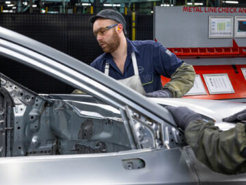 Een fabrieksarbeider die beschermende kleding draagt, inspecteert het interieur van een gedeeltelijk gemonteerd Nissan Qashqai-frame nabij een bedieningspaneel met het opschrift "Metal Line Check" in de fabriek in Sunderland.