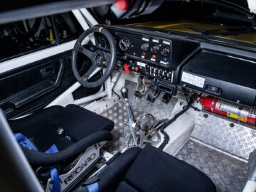 The interior of a rally car shows two bucket seats with harnesses, a metal floor, several gauges on the dashboard, a racing steering wheel, a gearshift and a floor-mounted fire extinguisher. This arrangement embodies the precision and dedication of motorsports.