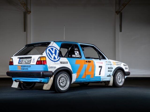 Rear and side views of a blue and white Volkswagen rally car marked with number 7 and bearing various sponsor logos, parked in a poorly lit area, capturing the essence of motorsports coverage.