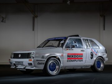 Inside, a white rally car with Nixdorf Computer and various sponsor logos is parked. The motorsports vehicle has a number 9 livery and mesh-style blue wheels, representing the essence of competitive excitement.