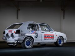 Een witte rallyauto met het opschrift 'NIXDORF COMPUTER' op de zijkant en logo's als 'Michelin' en 'Castrol', die binnen geparkeerd staat. Met zijn sportieve uiterlijk en gedetailleerde aanpassingen is dit op de Golfjes geïnspireerde voertuig een bewijs van de autosportwereld.