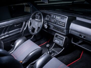 A well-kept vintage car interior with black leather seats, a manual shift lever and a dashboard with classic controls and a cassette player, reminiscent of the golden age of motorsports.