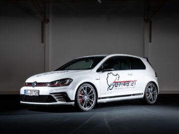 Inside, a white Volkswagen Golf GTI Clubsport S is parked, angled slightly to the right. The car features large alloy wheels, a front spoiler and race-inspired emblems on the side, exuding pure motorsport elegance.