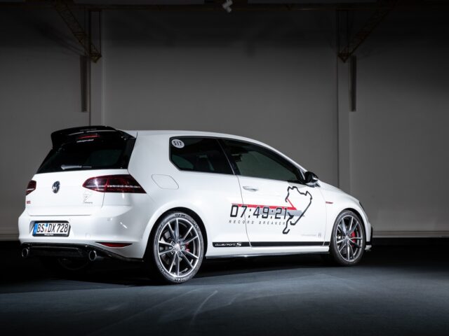 A white hatchback with graphics on the side, including the outline of the Nürburgring, is parked inside a dimly lit room. These sleek Golfs exude a motorsport atmosphere, perfect for any reportage capturing powerful vehicles.