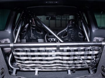 Interior view of the rear compartment of a car with two racing seats, a roll cage and a safety harness net, indicating modifications for safety in motor racing.