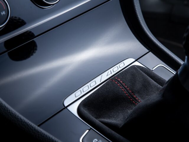 Close-up of the switch area of a car with black leather upholstery with red stitching. The panel is numbered 